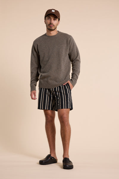 A man stands against a beige background wearing Barkers’ Lawton Stripe Short with an elasticated waistband, a brown sweater, black slip-on shoes, and a brown cap. He has one hand in his pocket and looks at the camera neutrally.