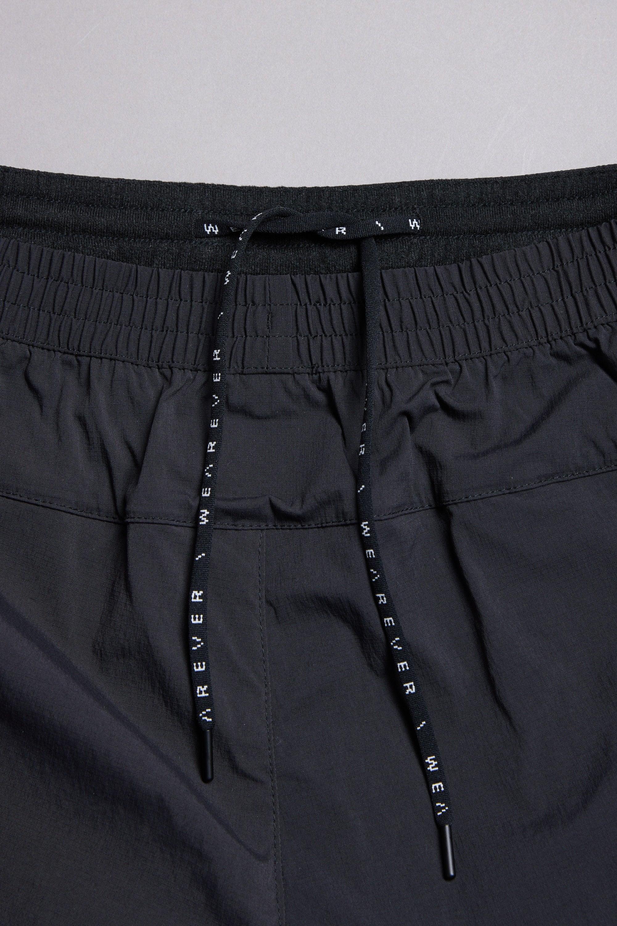 Close-up of the WearEver Agile Short's black elastic waistband, featuring gathered elastic and two black drawstrings with white "WEAR EVER" text from the WearEver brand.