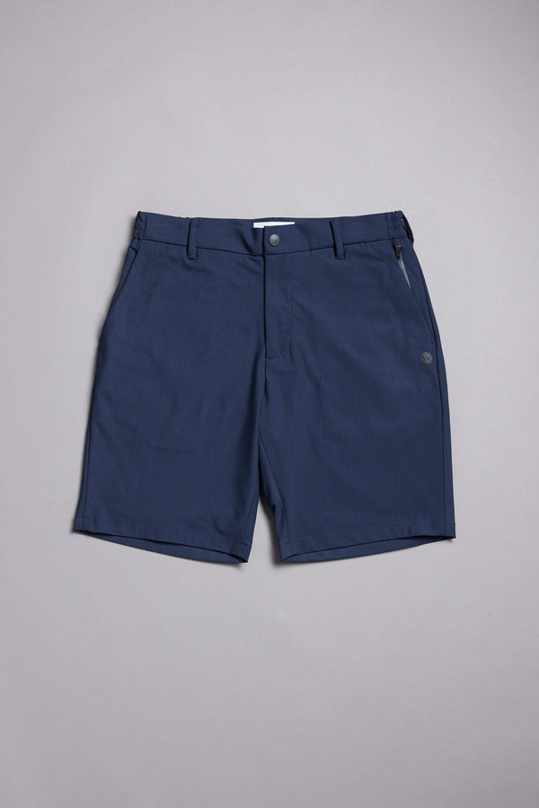 The WearEver Switch Short by WearEver is a pair of navy blue chino-style shorts featuring belt loops, a front button and zipper, plus a zippered right pocket, shown laid flat on a light gray surface.