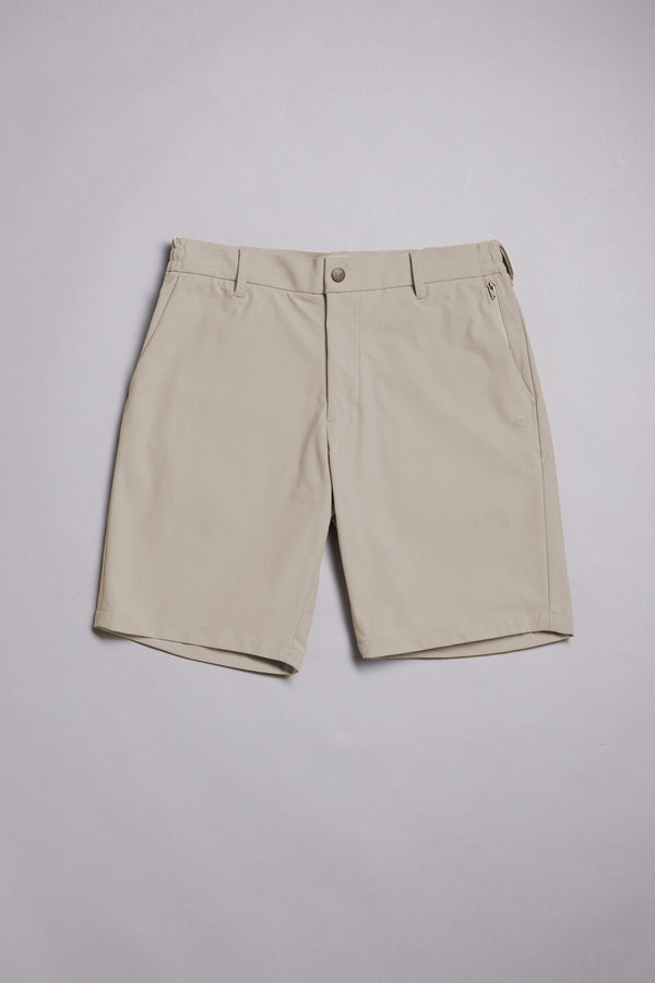 The WearEver Switch Short by WearEver is a beige, knee-length performance short with comfort stretch, belt loops, two side pockets, a zippered right pocket, and button closure, shown laid flat on a light gray background.