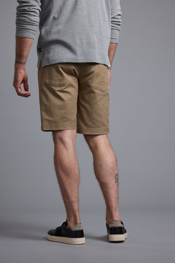 A person faces away, wearing a light gray long-sleeve shirt and the Barkers Anvil 5Pkt Short with an elasticated waistband. Black sneakers complete the look, revealing tattooed lower legs against a plain gray background.