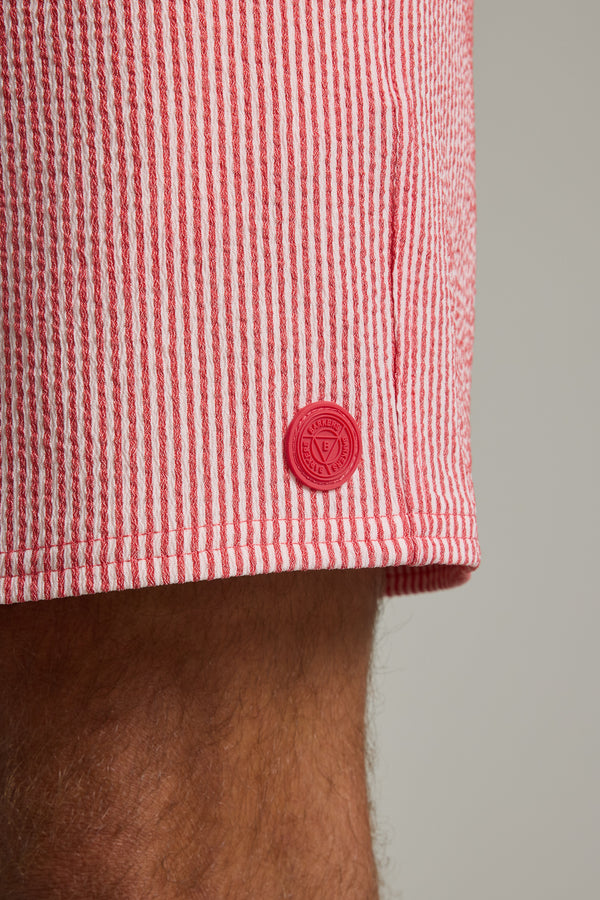 Close-up of Barkers Dehaven Stripe Volley shorts in red and white seersucker, featuring a small round red logo patch near the hem, worn by a person with visible leg hair.