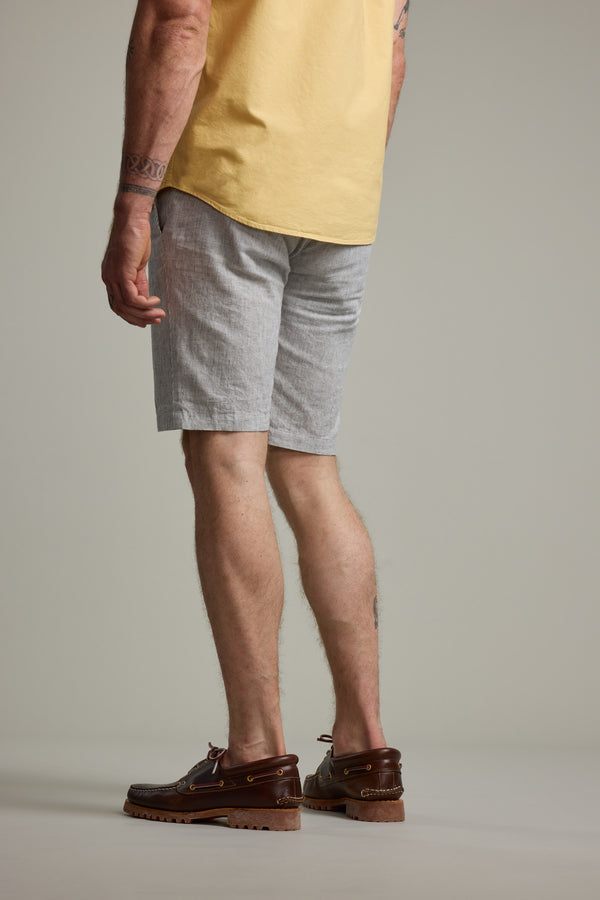 A person stands facing away, showing only their lower back, legs, and a tattooed arm against a plain background. They wear Barkers' Palma Walkshort in light gray with a yellow short-sleeve shirt and brown boat shoes.