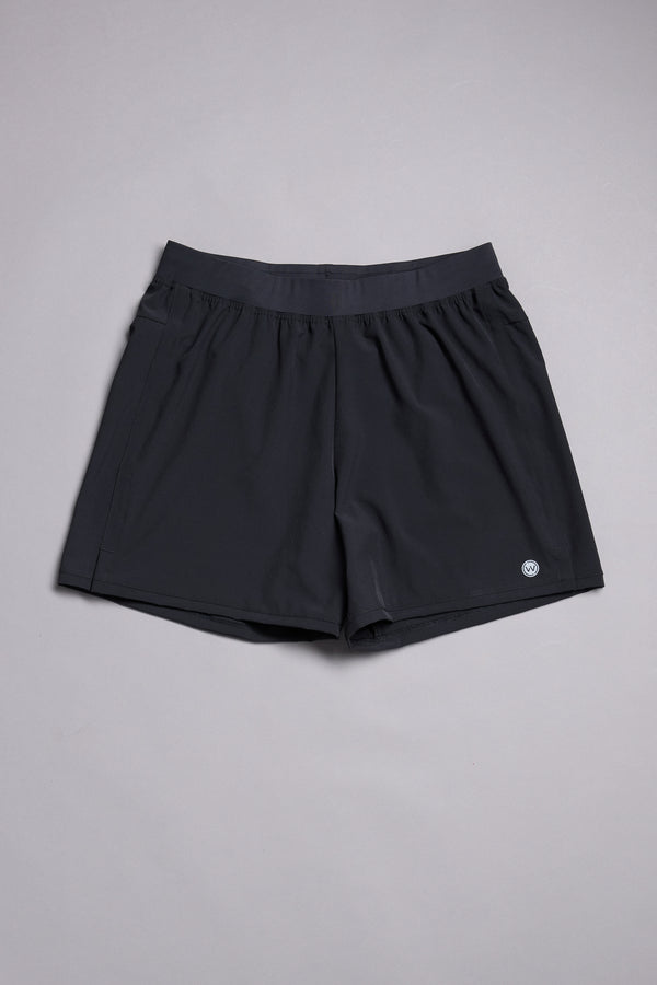 The WearEver Cadence Short, a pair of lightweight black workout shorts with a 5-inch inseam and elastic waistband, is laid flat on a light gray surface. A small round WearEver logo appears near the bottom hem on one leg.