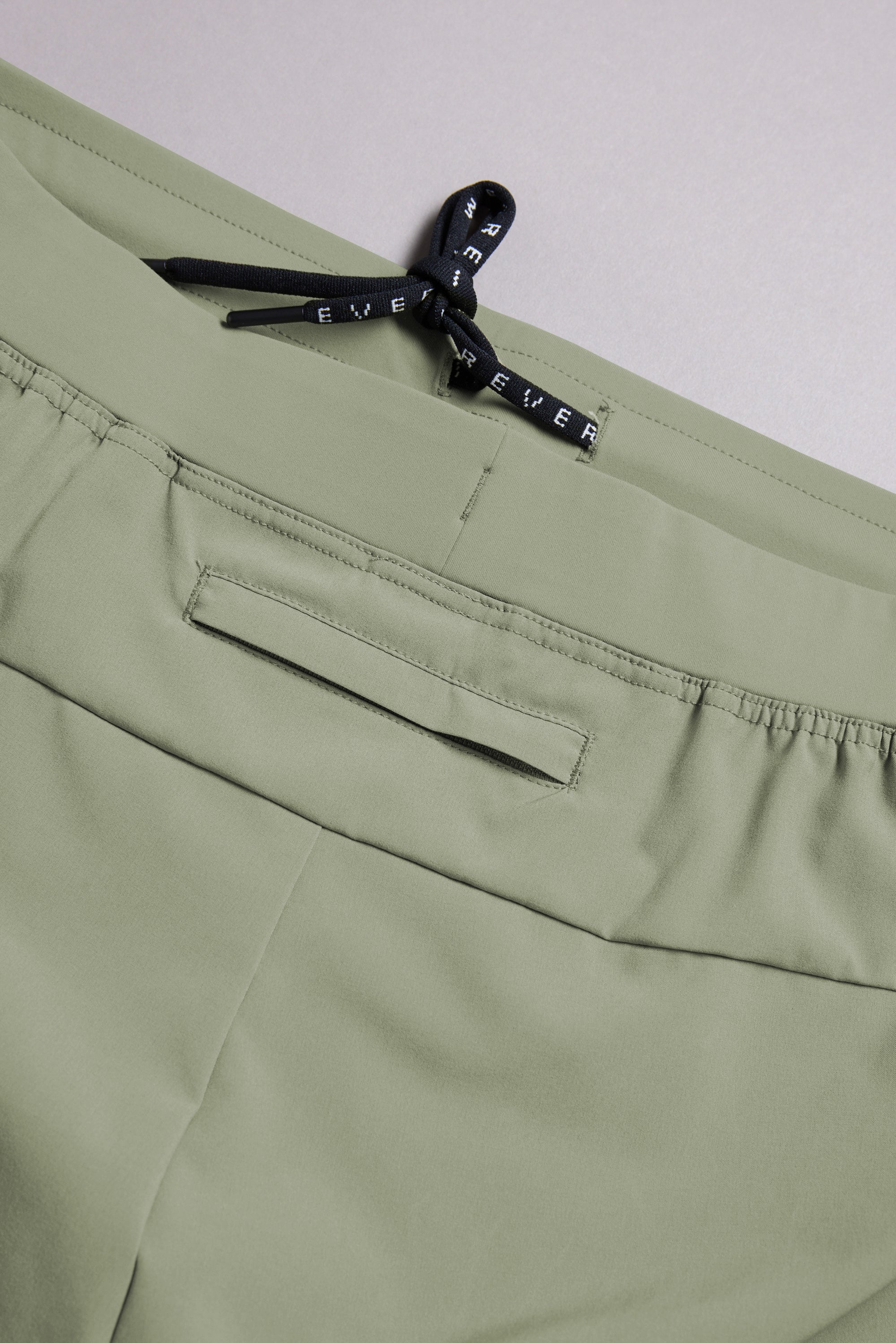 Close-up of light green WearEver Cadence Short featuring an elastic waistband, black drawstring bow, and horizontal back pocket. Made from lightweight, breathable fabric with a 5-inch inseam for comfort.