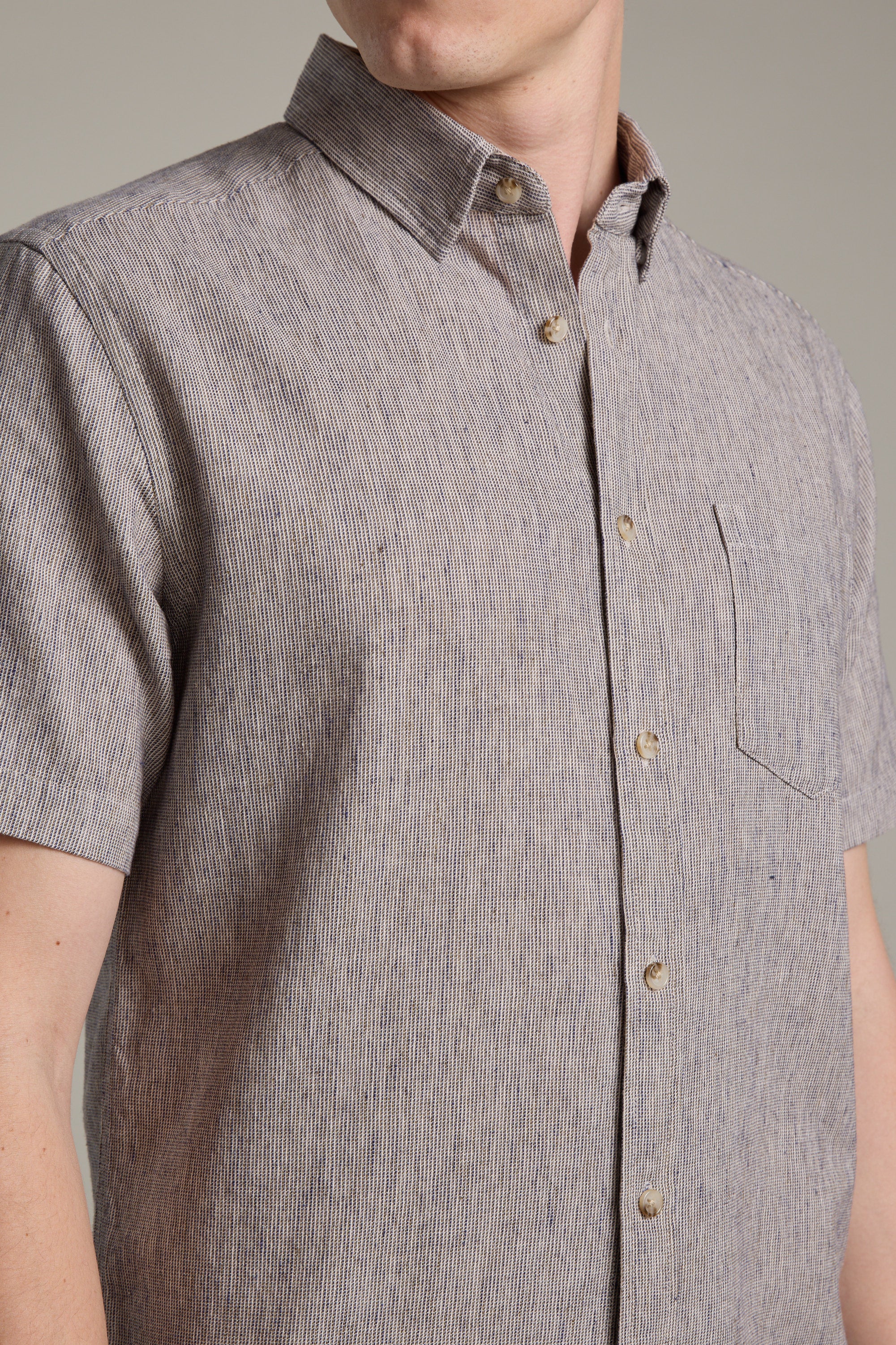 A person is seen from shoulders to waist wearing the Barkers Woodley Texture Shirt, a short-sleeved button-up featuring a subtle vertical stripe pattern and front pocket.