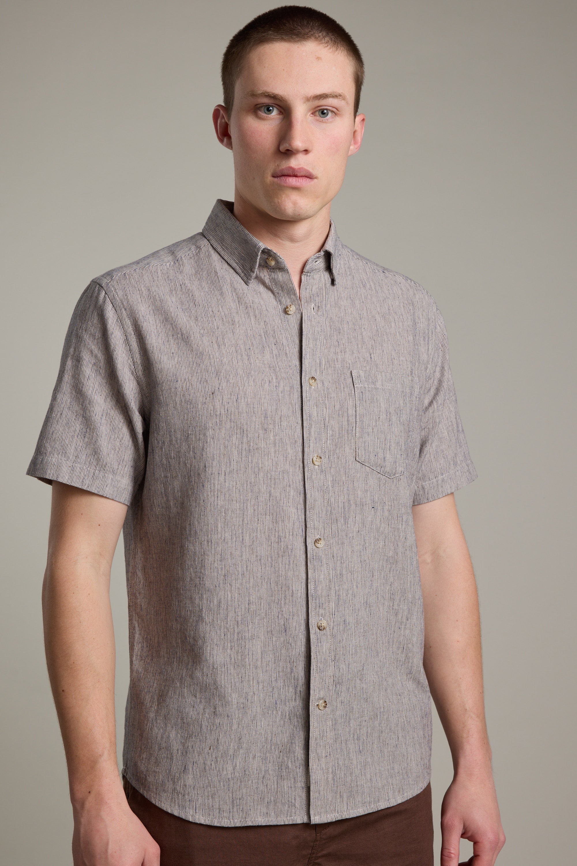 A man wearing a short-sleeve, light gray Barkers Woodley Texture Shirt with a chest pocket stands facing the camera against a plain, light background.