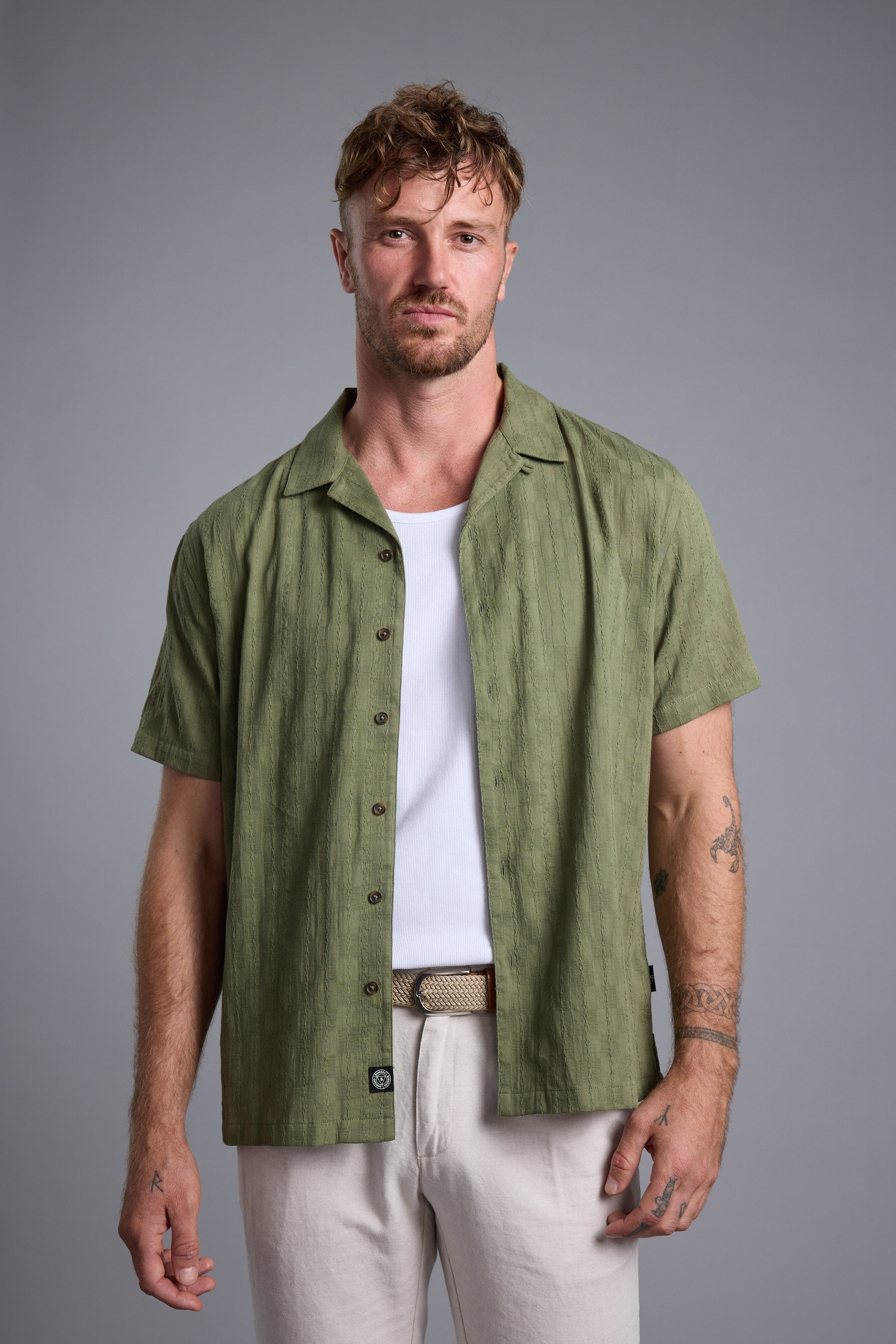 Man in a green Otis Stripe Cuban Shirt by Barkers over a white tank and beige pants, facing forward.