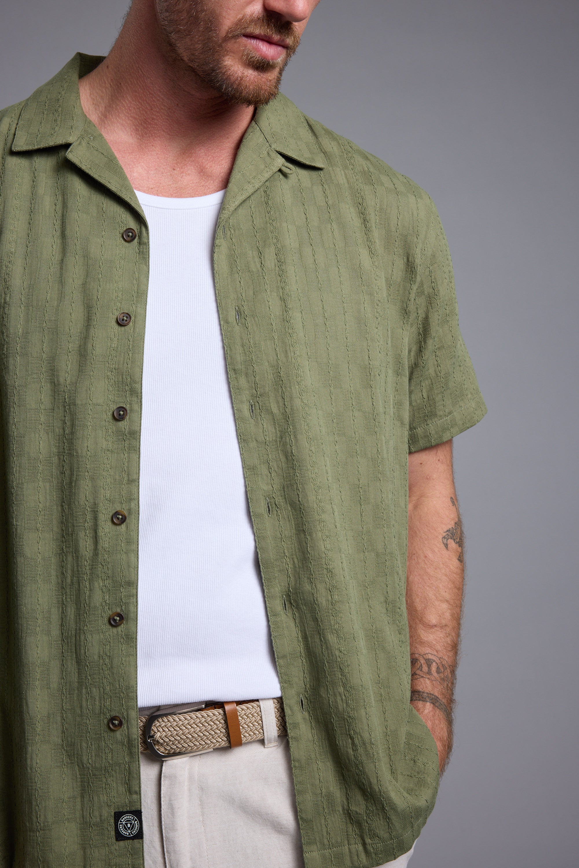 Man wearing a Barkers Otis Stripe Cuban Shirt over a white tank and beige belted pants.