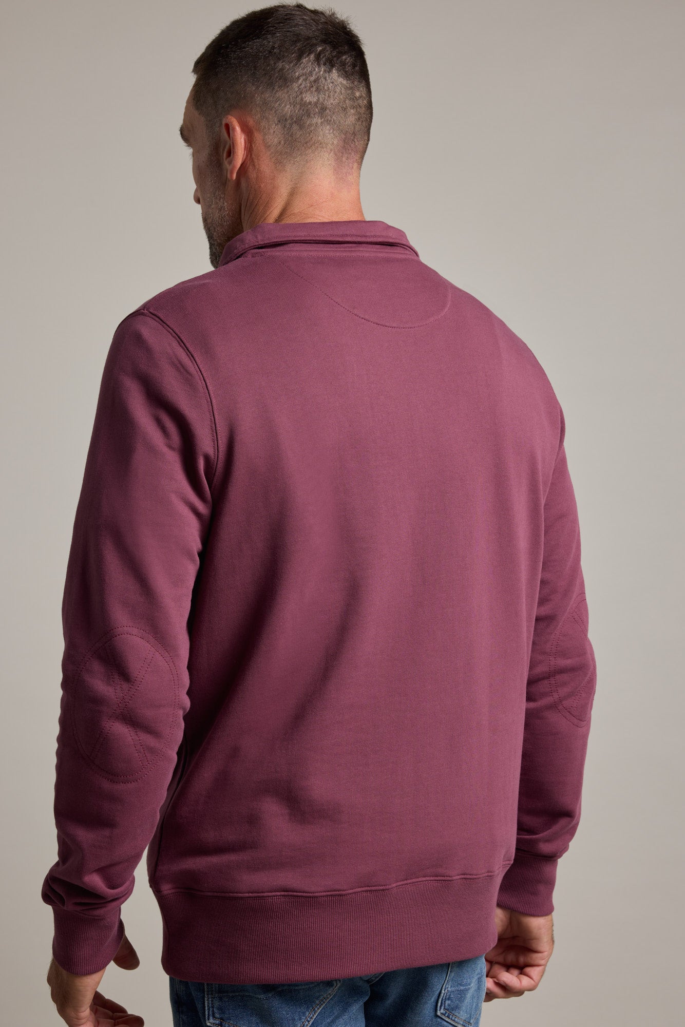 A man is seen from the back in a Barkers Heritage 1/4 Zip sweater by Barkers, paired with blue jeans, standing against a plain light background.