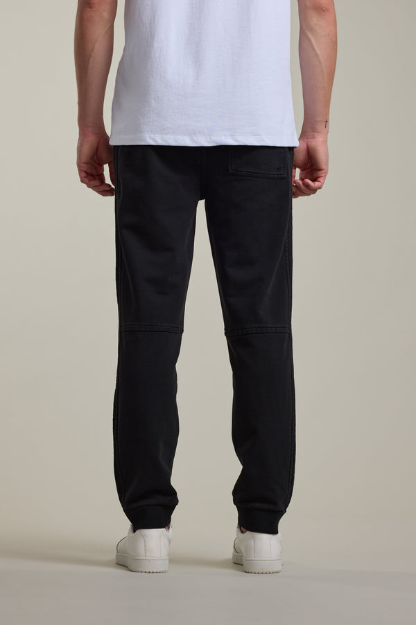 A person stands with their back to the camera, wearing Barkers' Organic Classic Print Track Pant and a white t-shirt with white sneakers, set against a plain light background.