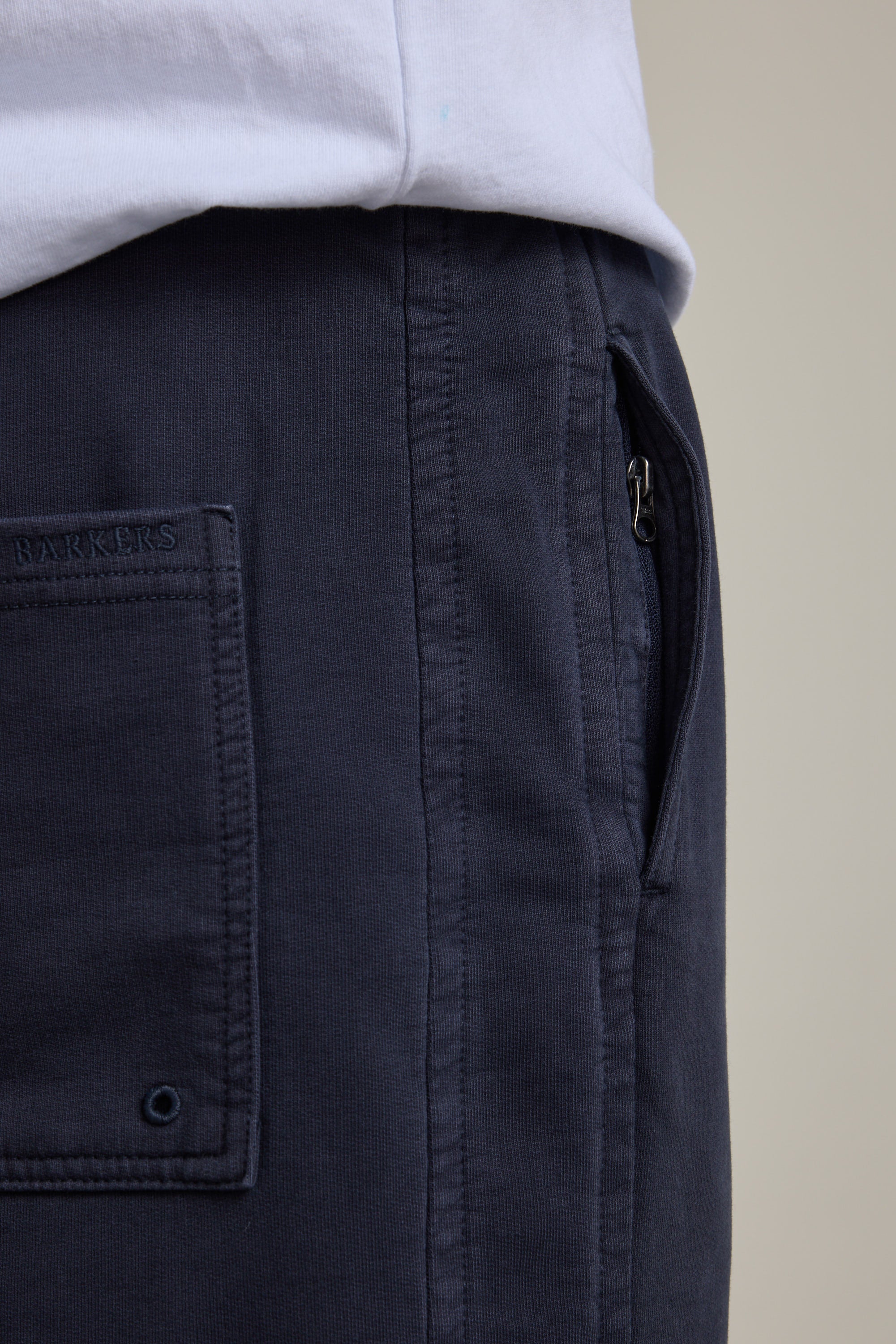 Close-up of a person wearing Barkers Organic Classic Print Track Pant in navy blue, featuring a side zipper pocket and visible back pocket, paired with a white shirt neatly tucked at the waist.