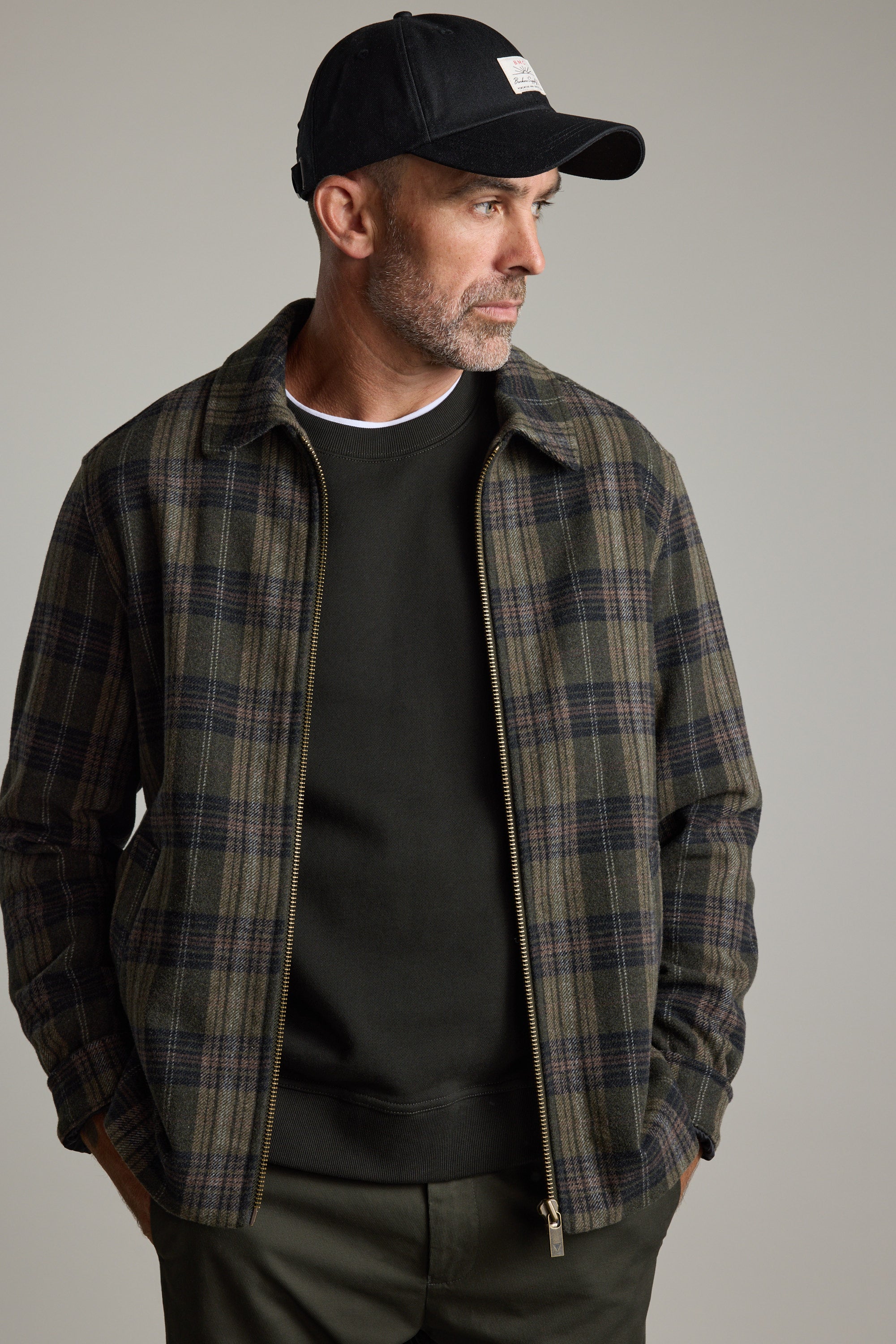 Man in a Barkers Zermatt Wool Jacket and black cap looks to the side, hands in pockets.
