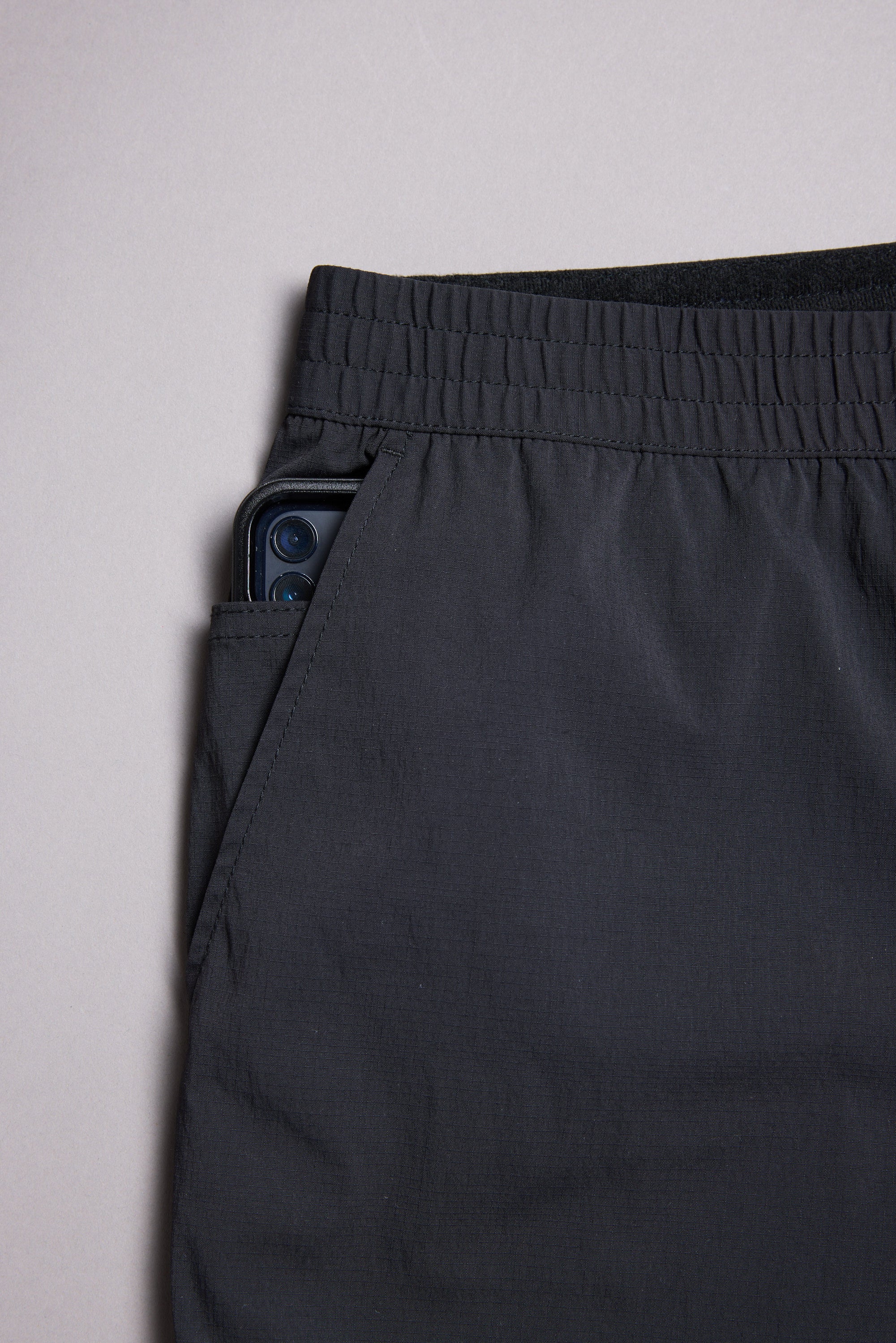 The WearEver Transit Pant by WearEver is a black, lightweight travel pant with an elastic waistband, shown on a plain background. A smartphone peeks out from the pant’s side pocket.