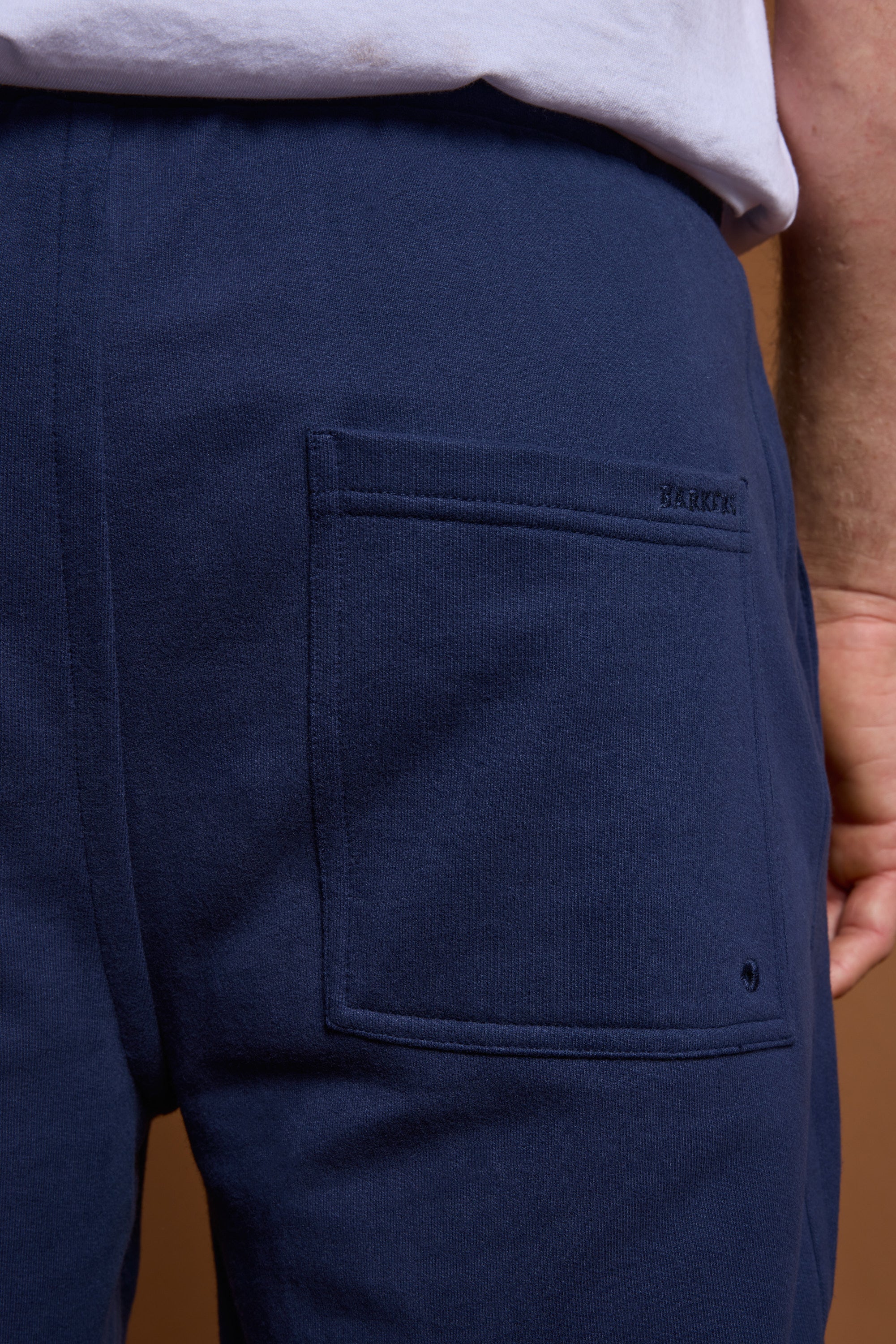 Close-up of a person wearing the Barkers Heritage Track Pant in navy blue, with a back pocket featuring BARUCCK stitching. Paired with a white shirt, this Barkers look blends comfort and classic style.