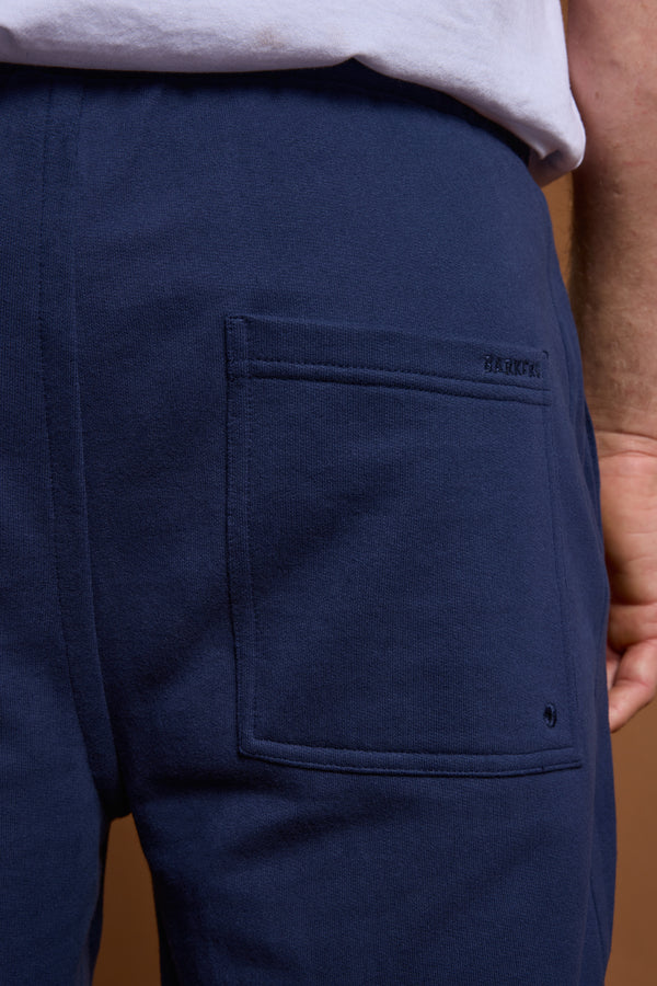 Close-up of a person wearing the Barkers Heritage Track Pant in navy blue, with a back pocket featuring BARUCCK stitching. Paired with a white shirt, this Barkers look blends comfort and classic style.