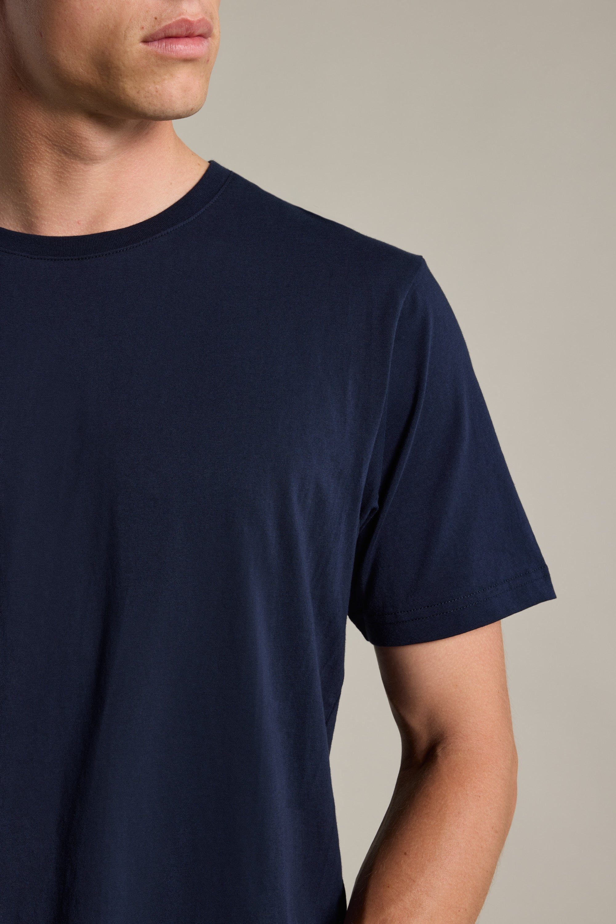 A man models the Barkers Organic Crew Tee in plain navy blue, crafted from 100% organic cotton; only his lower face, upper torso, and right arm are visible against a neutral background.