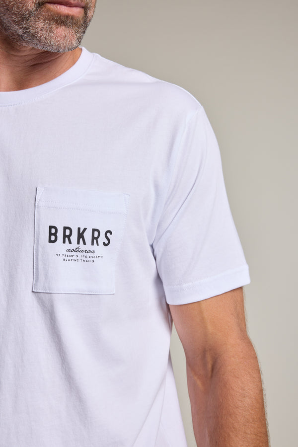 A man wears the Barkers Basecamp Logo Tee by Barkers, a white organic cotton T-shirt with a chest pocket and “BRKRS authentic” print. Only his lower face and upper body are shown—an essential piece for any Kiwi wardrobe.