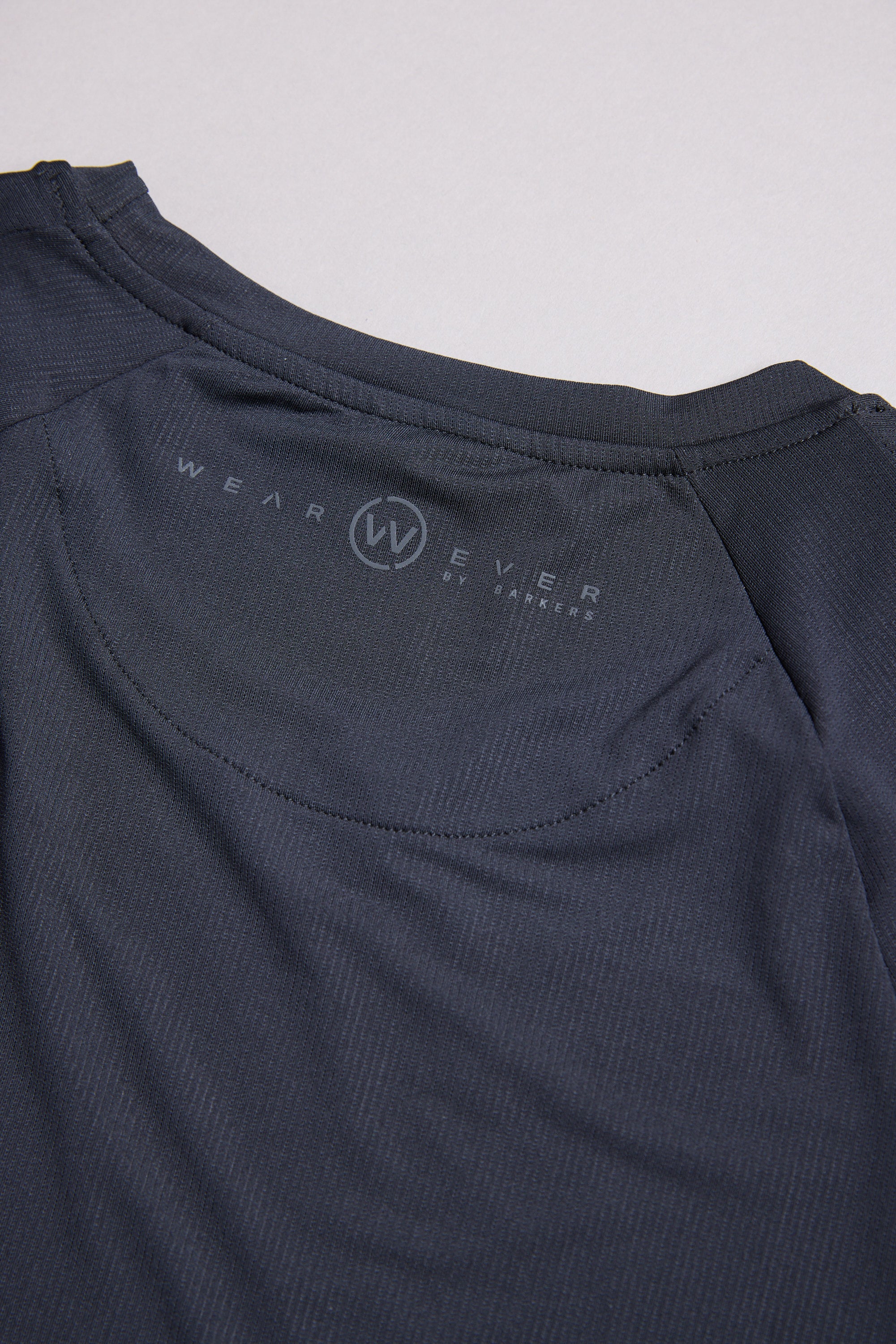 Close-up of the back neckline of the WearEver Pulse Long Sleeve Tee, featuring the WearEver logo and text printed inside the collar. The dark, moisture-wicking fabric looks lightweight and slightly textured.
