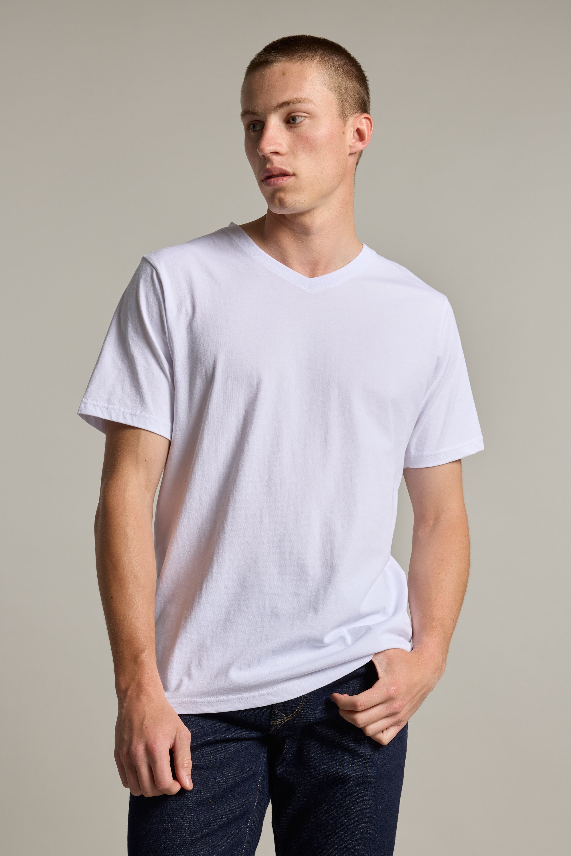 A young man models the Barkers Organic Cotton V Neck Tee with dark jeans, standing against a neutral background. He looks to the side, relaxed, with one hand in his pocket.