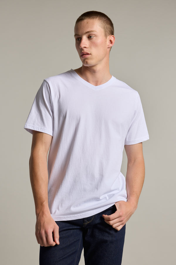 A young man models the Barkers Organic Cotton V Neck Tee with dark jeans, standing against a neutral background. He looks to the side, relaxed, with one hand in his pocket.