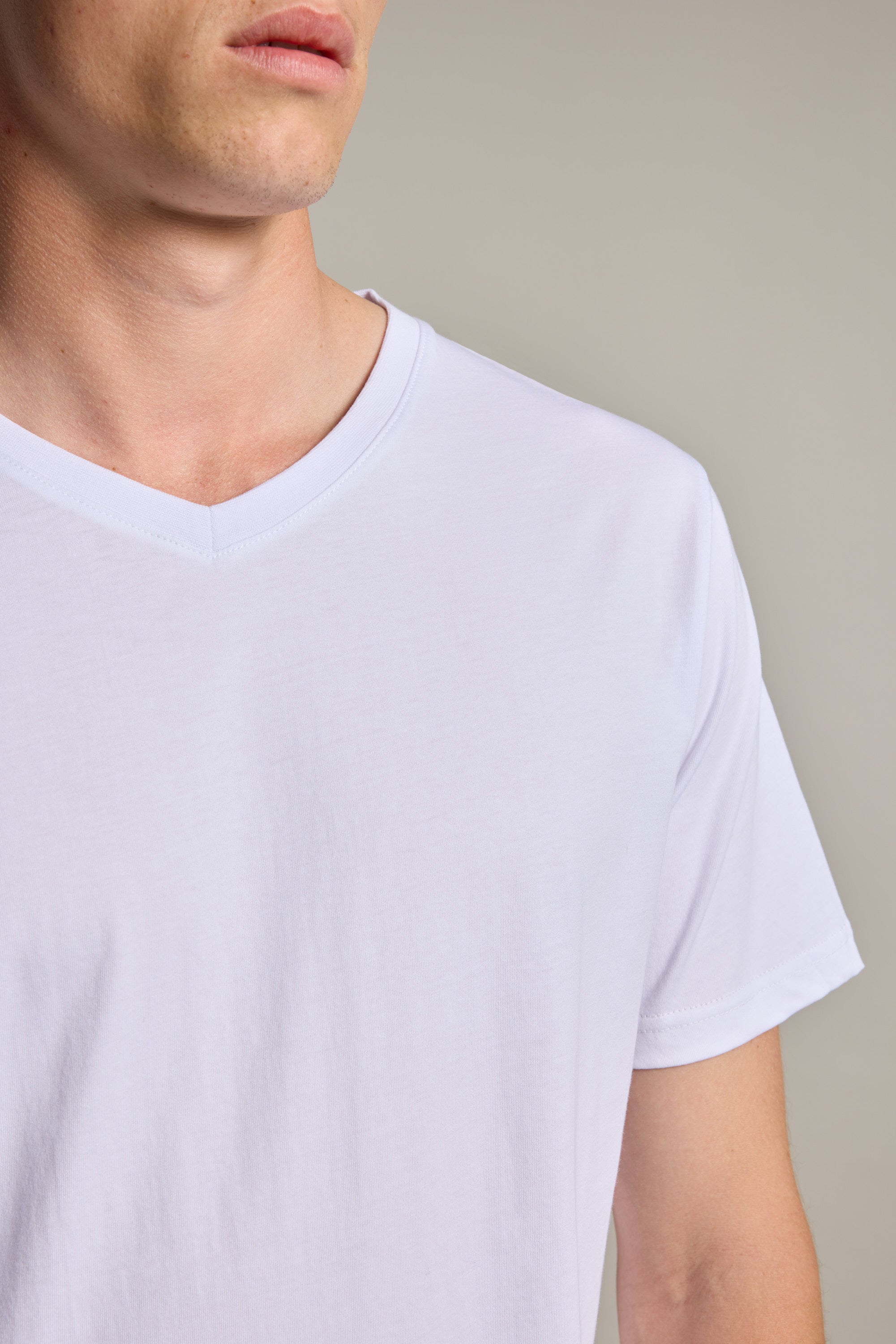 A close-up shows the lower face, neck, and upper torso of a person wearing the Barkers Organic Cotton V Neck Tee in plain white, set against a neutral background.