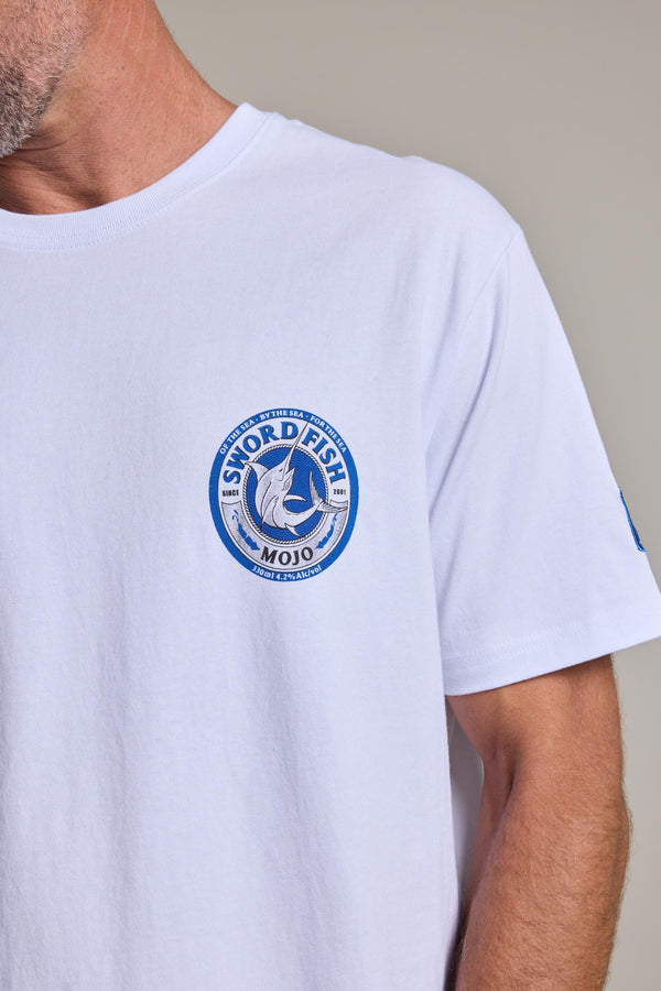A person wears the Swordfish Mojo Logo Tee, an organic cotton shirt from Swordfish Mojo, featuring a blue circular chest logo with a swordfish and “Sword Fish Mojo” text; their head is partially out of frame.