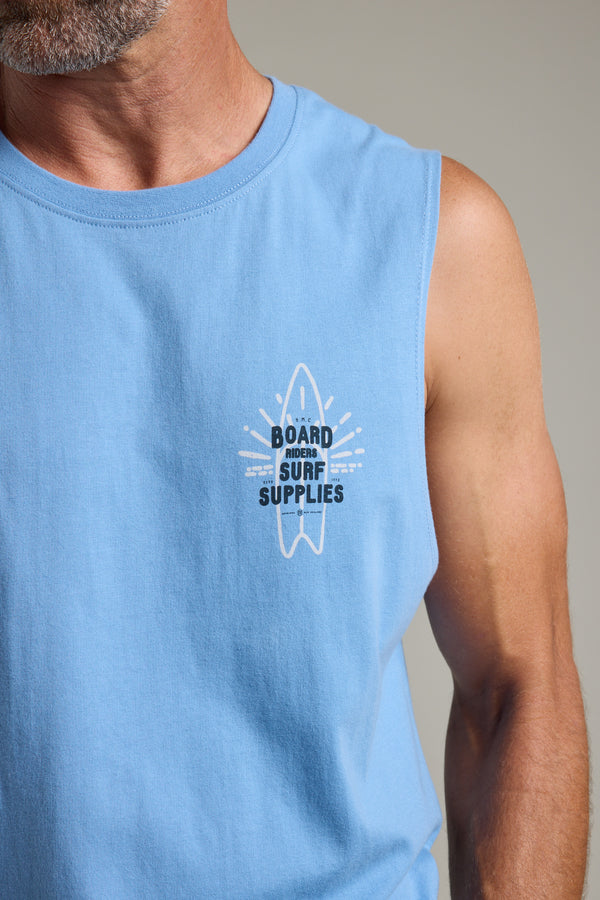 A man wears the Barkers BMC Board Riders Print Singlet in light blue, featuring a white surfboard graphic and "BOARD MOVER SURF SUPPLIES" text on the upper left chest—a true summer staple.