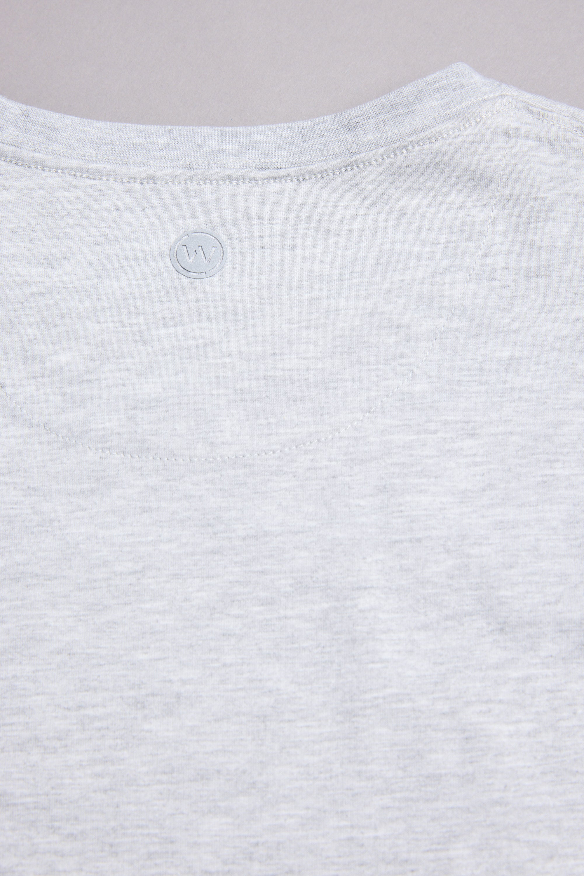Close-up of the WearEver Outbound T-Shirt's upper back in light grey, featuring a subtle stitched WearEver logo near the neckline against a plain background.