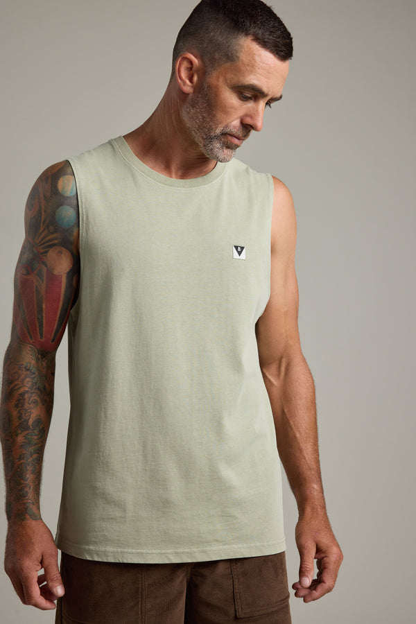 A man with short dark hair and a gray beard wears the Barkers Newton Washed Singlet in light green, featuring a vintage feel. He pairs it with brown shorts and has a tattooed left arm, looking down neutrally against a plain background.