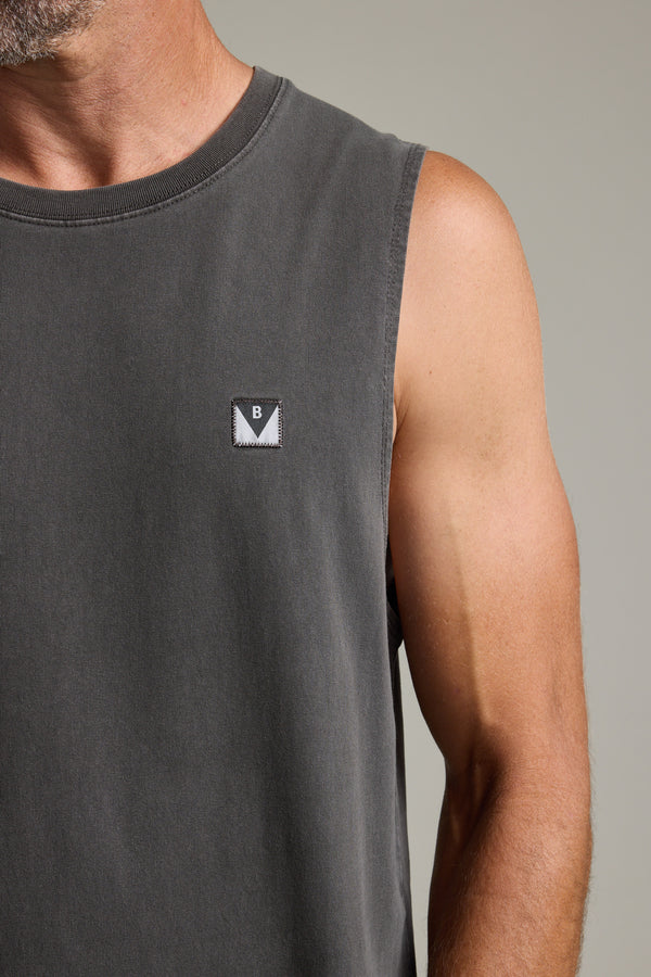A close-up shows a person wearing the Barkers Newton Washed Singlet, an oversized sleeveless dark gray top with a small rectangular B patch on the chest. Only their lower face, shoulder, and upper arm are visible.