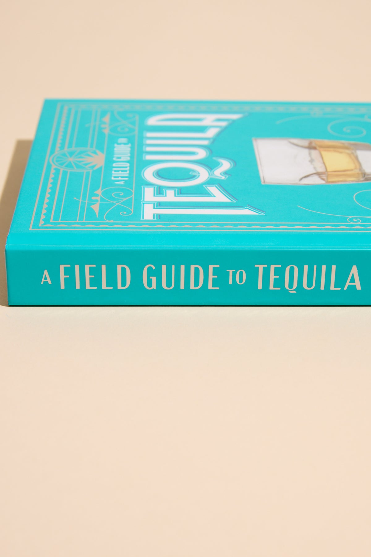 Other’s A Field Guide To Tequila, a turquoise book, rests on a beige surface.