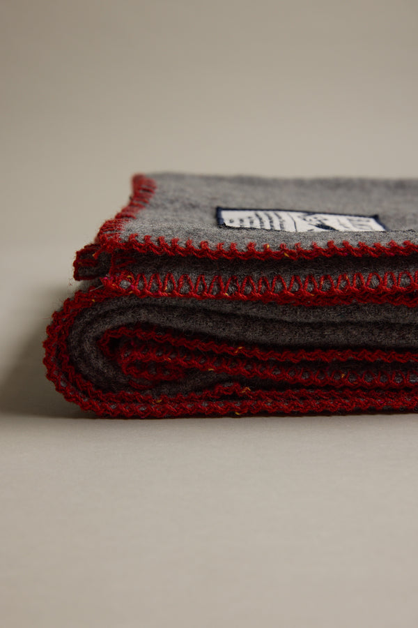 Other Wool Take Back Blanket, gray recycled wool with red stitching, folded on a plain surface.