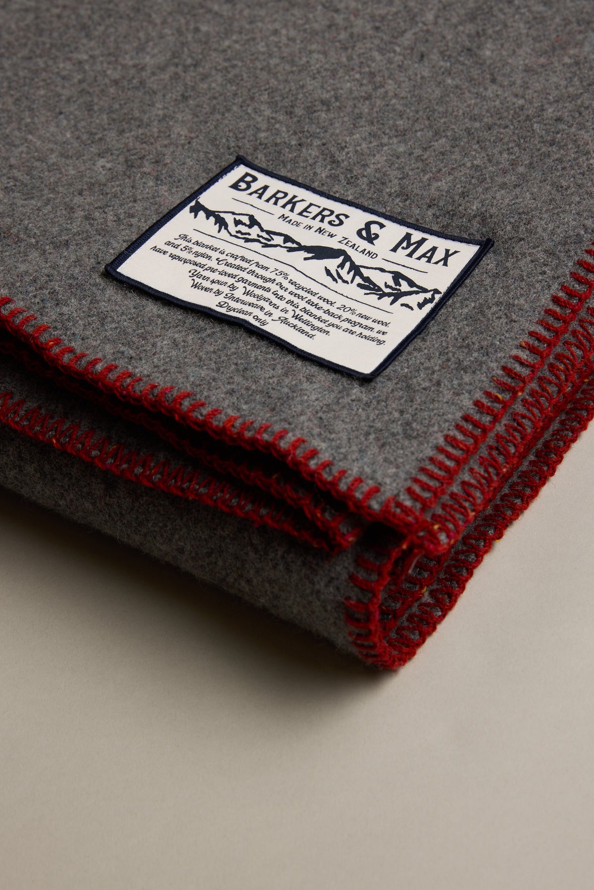 Folded gray Wool Take Back Blanket by Other, with red stitching and a Barkers & Max label on top.