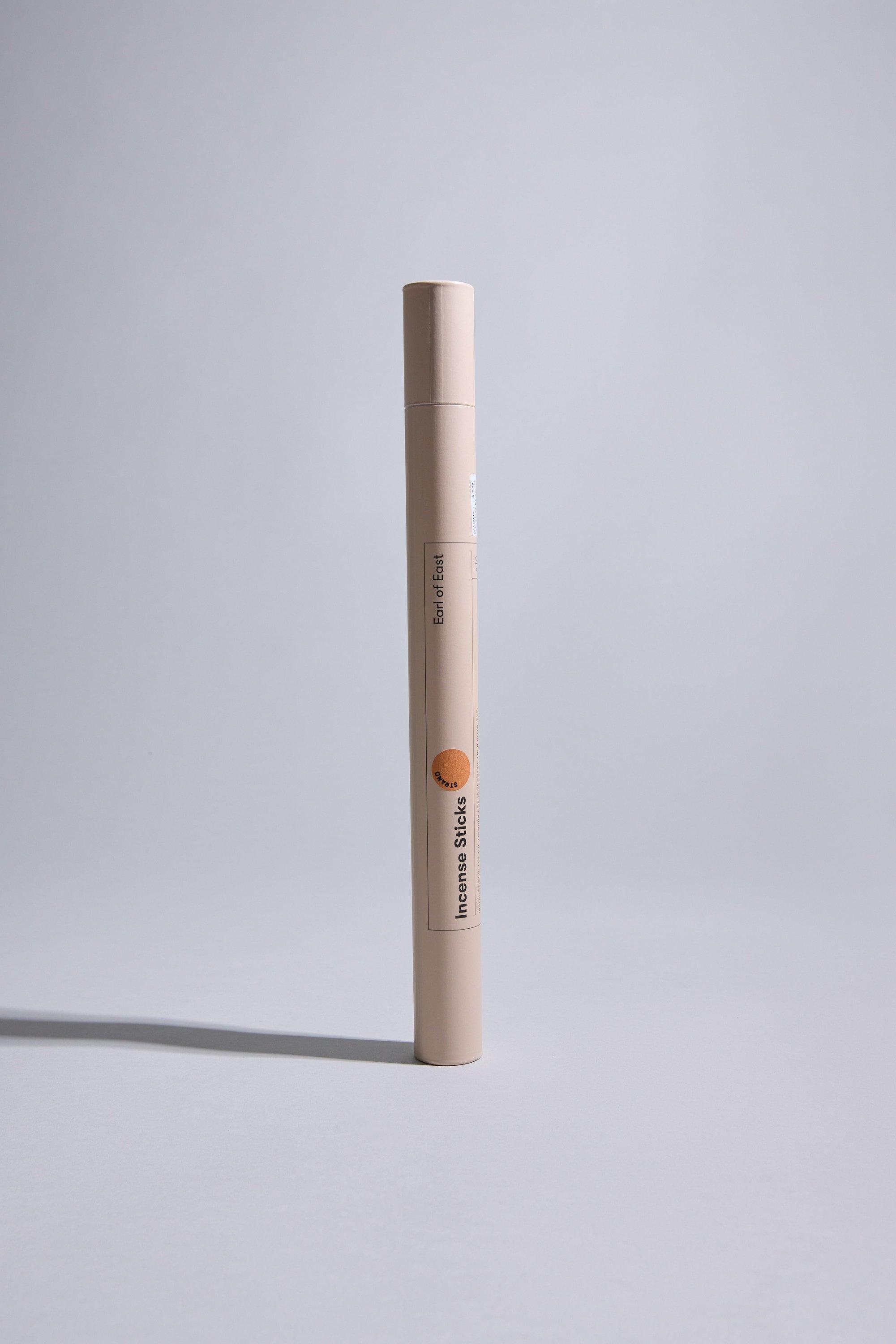 A vertical beige cylindrical container labeled "EoE Strand Incense Sticks" by Earl of East, with mandarin and birchwood scented incense, stands upright on a light grey surface against a plain light grey background.