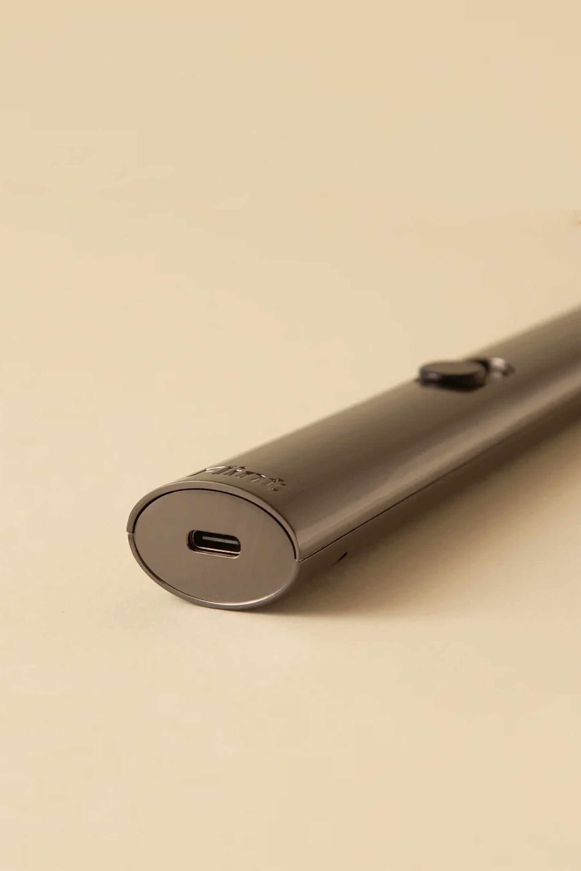 A close-up of the Flint Rechargeable Lighter 2.0 by Flint, featuring a sleek metallic design, USB-C charging port, and a small side button, resting on a beige surface.