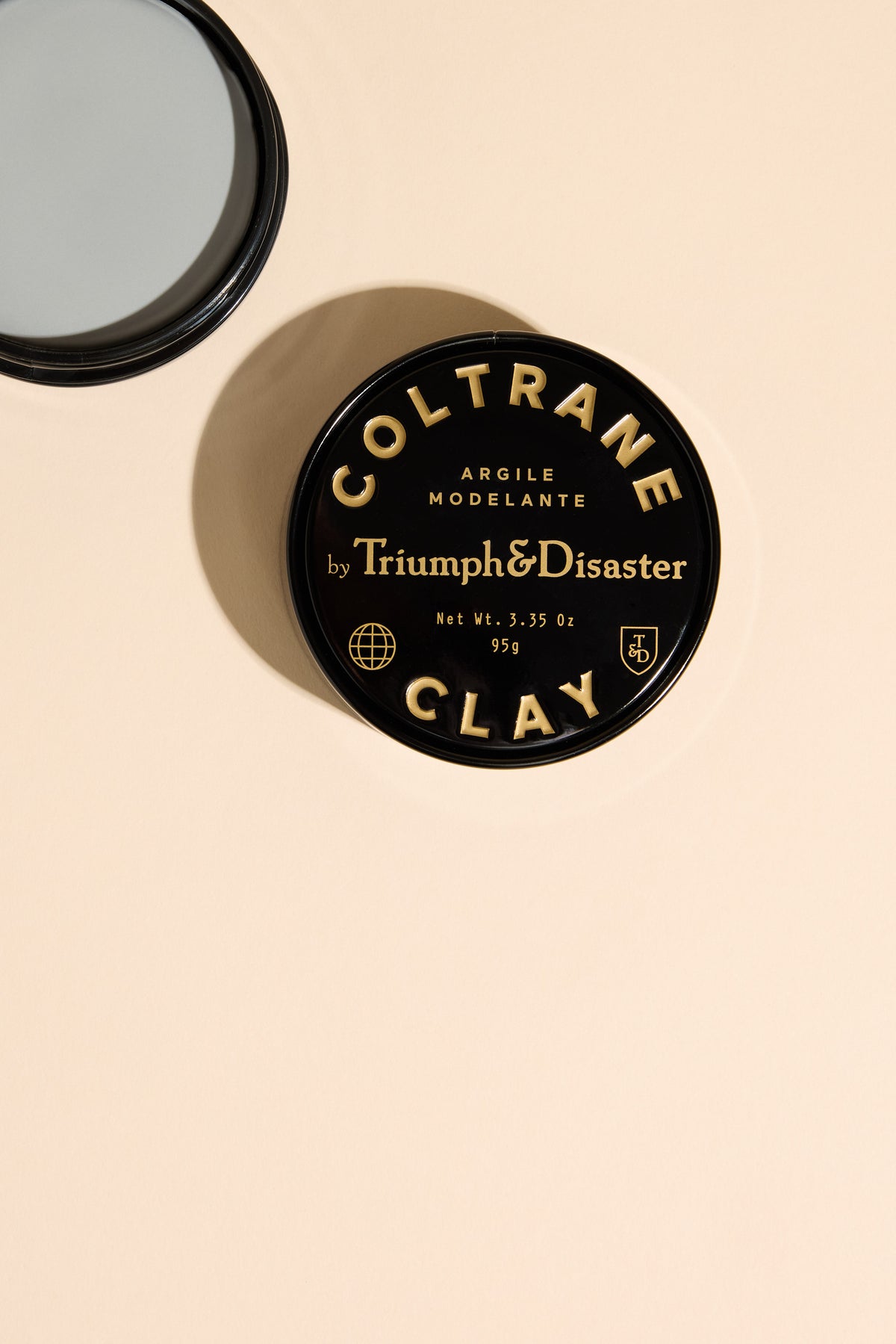 Triumph & Disaster Coltrane Clay: matte medium hold clay tin on beige with round mirror.