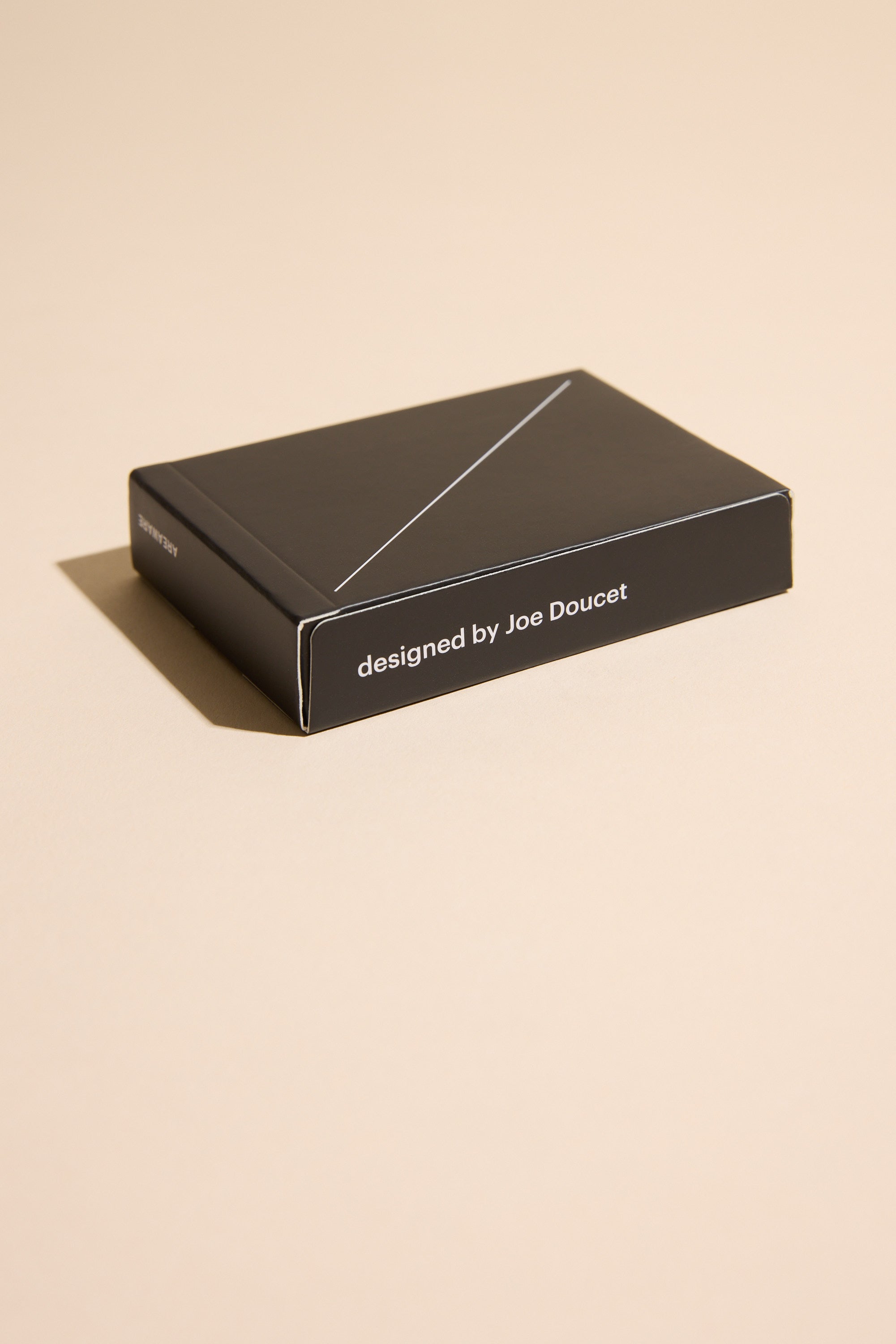 A sleek black box labeled “designed by Joe Doucet” sits on a beige surface with a left shadow, hinting at the elegant Minim Playing Cards inside from Other.