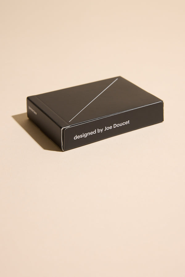 A sleek black box labeled “designed by Joe Doucet” sits on a beige surface with a left shadow, hinting at the elegant Minim Playing Cards inside from Other.