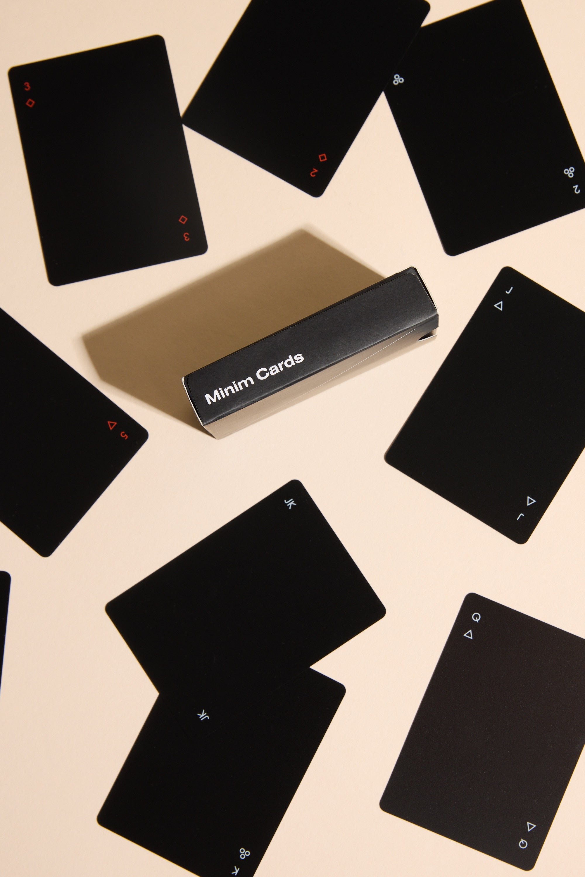 Minim Playing Cards by Other feature black faces with small white or red suit and value symbols, packed in a sleek black Minim Cards box, arranged on a light beige surface for a modern look.
