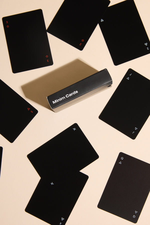 Minim Playing Cards by Other feature black faces with small white or red suit and value symbols, packed in a sleek black Minim Cards box, arranged on a light beige surface for a modern look.