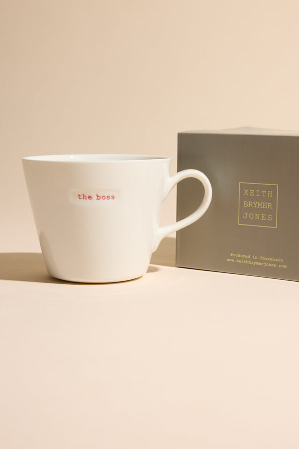 Bucket Mug - The Boss by Other next to its gray box on a beige surface.