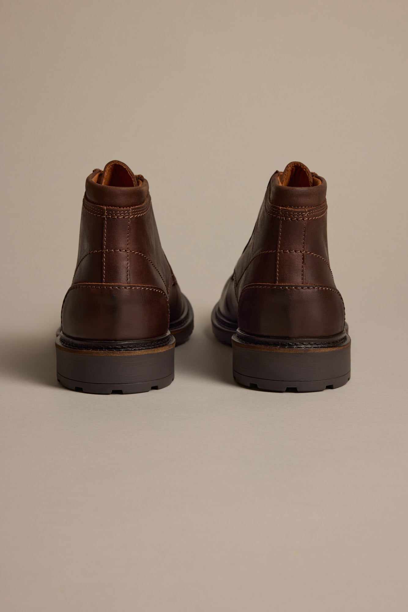 The Carlton Boot by Barkers—brown Italian leather ankle boots, shown from the back and side by side on a light beige surface—offers men a luxury footwear option.