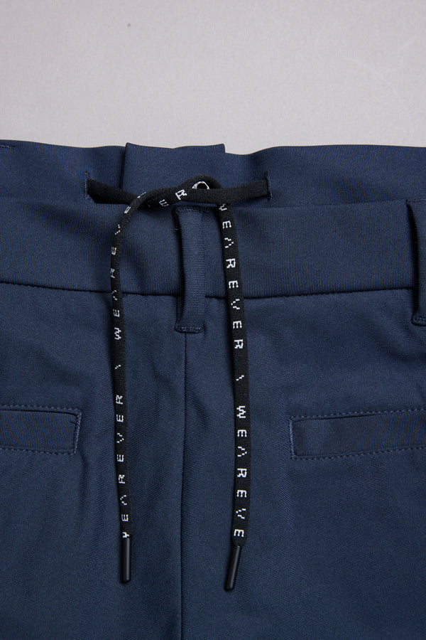 Close-up of the WearEver Long Game Pant: navy performance travel pants with an elastic waistband, black drawstring with white WEAR EVER text, two back welt pockets, and a chino-inspired design.