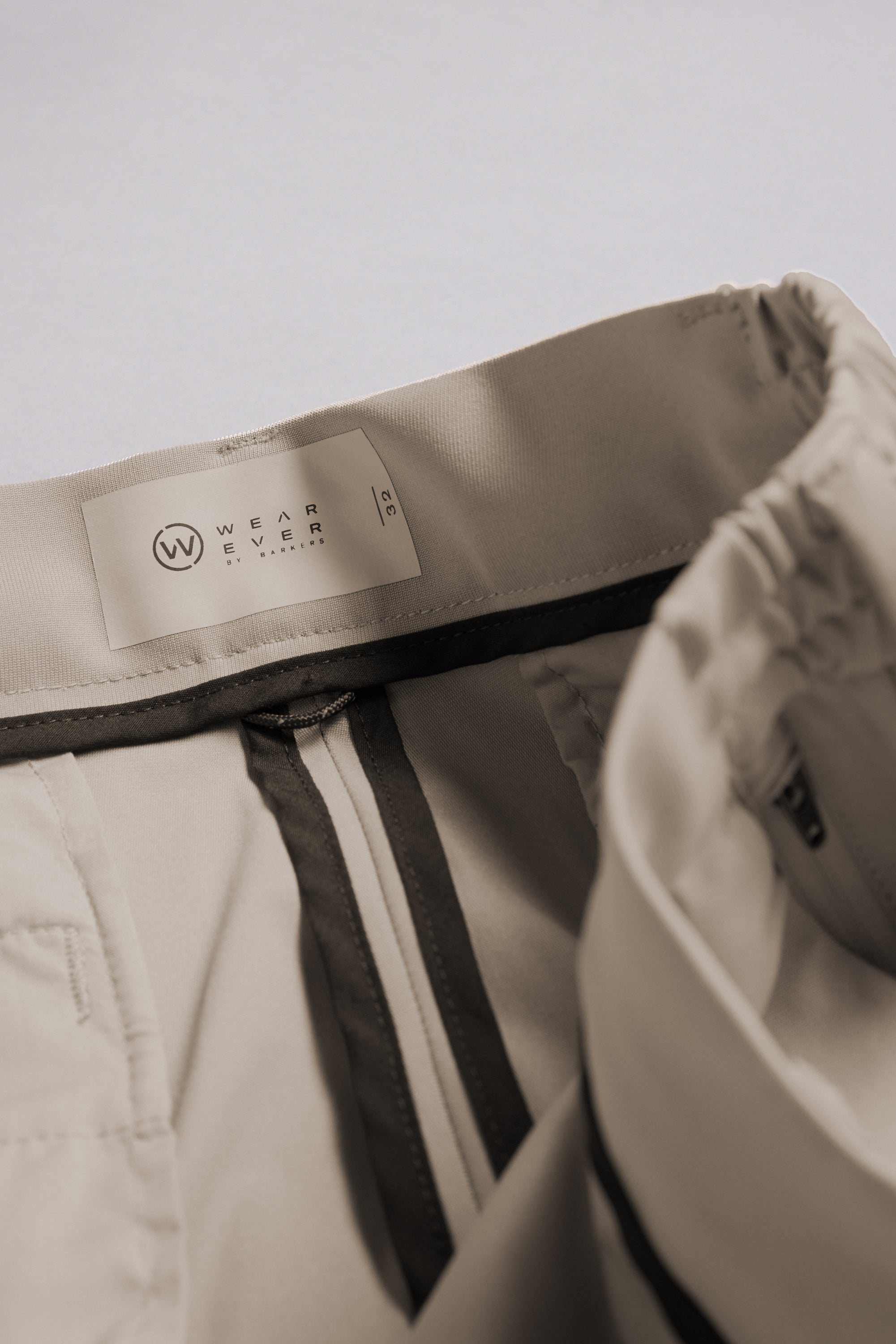 Close-up of the waistband and inside label of light beige WearEver Switch Short by WearEver, size L. These performance shorts feature an elastic waistband, zipper, and comfort stretch for all-day comfort.