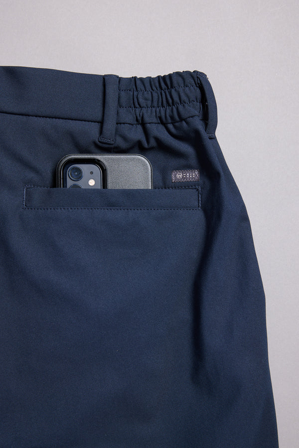 The WearEver Long Game Pant by WearEver is a navy blue, lightweight performance pant with an elastic waistband and a back pocket fitting a black smartphone, featuring chino-inspired design and shown on a light grey background.