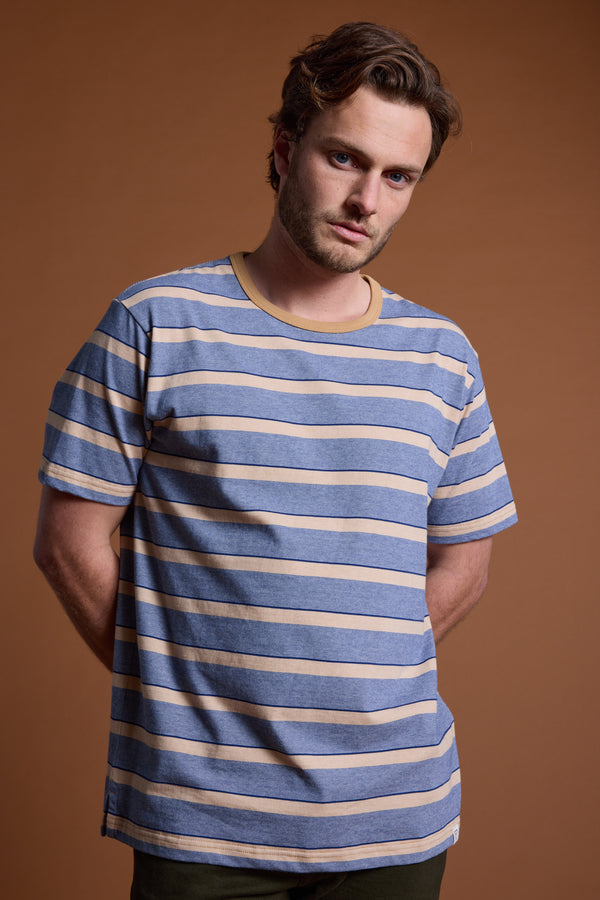 A man with wavy brown hair and a short beard stands against a brown background, wearing the Barkers Chester Stripe Tee, looking directly at the camera with a neutral expression.