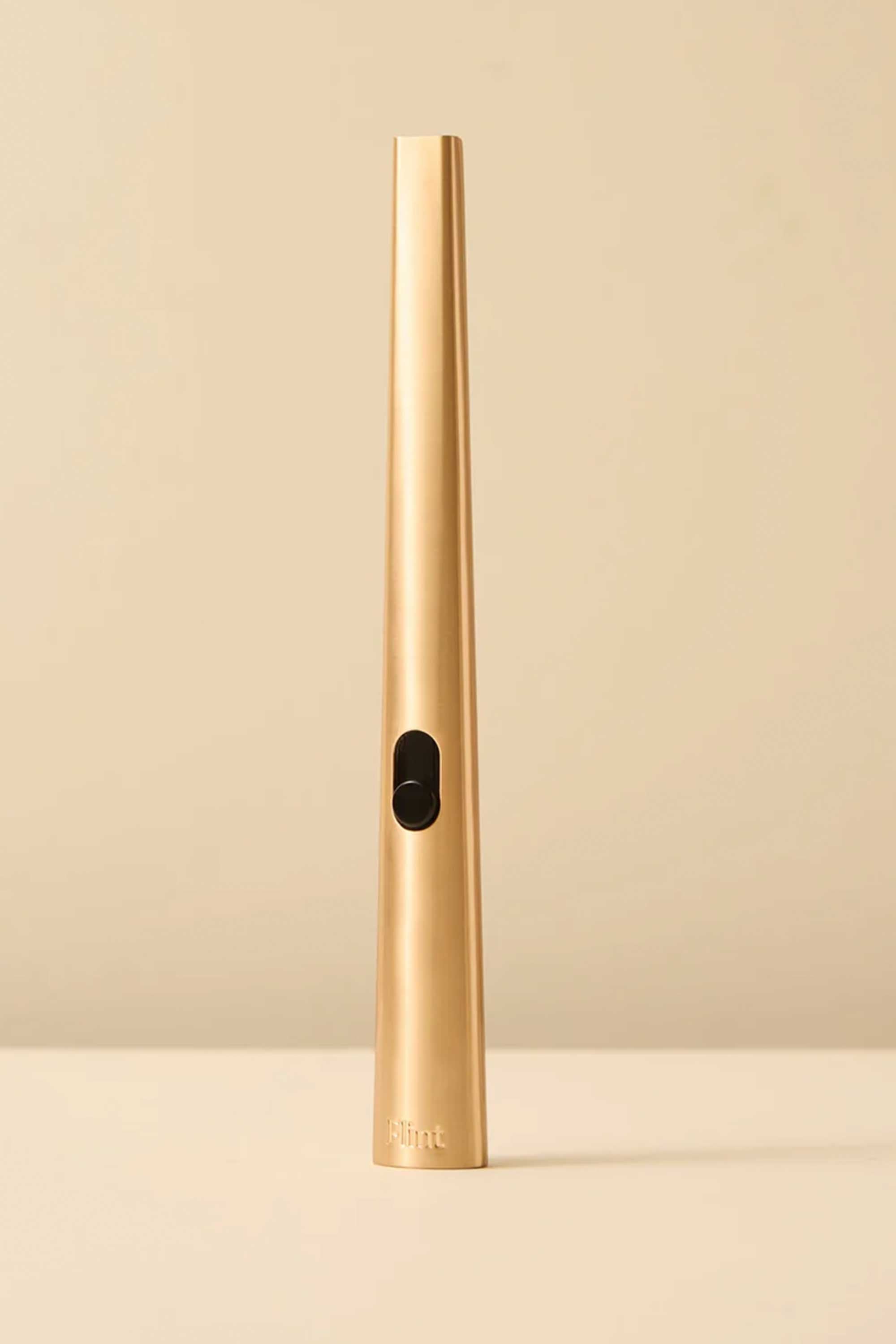 The Flint Rechargeable Lighter 2.0 by Flint features a sleek, gold cylindrical and tapered design, standing upright on a beige surface with a matching beige background.