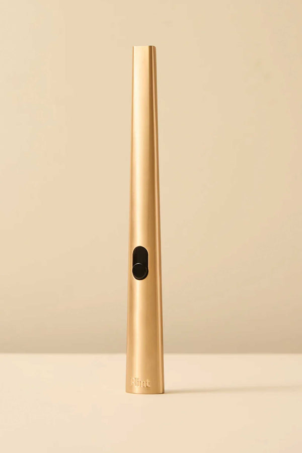 The Flint Rechargeable Lighter 2.0 by Flint features a sleek, gold cylindrical and tapered design, standing upright on a beige surface with a matching beige background.